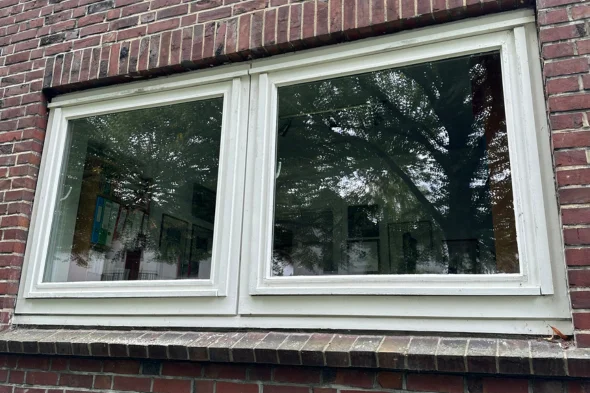 Holzkonzept-Vorher-Nachher-Fenster-Fenstertausch-1 Zweiflügelfenster mit weißem Rahmen und Baumbildung reflektiert, eingebaut in eine rote Backsteinmauer.